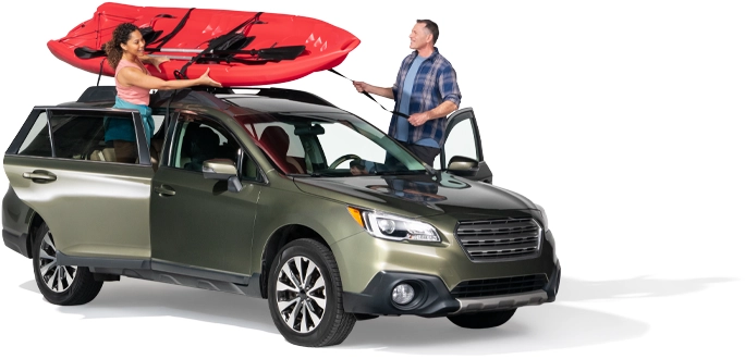 A couple secure a red raft atop their SUV