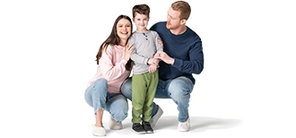 Mom and Dad kneel next to their son. He stands there smiling in a grey shirt and green pants.