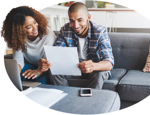 A smiling couple sitting on a grey sofa review a printing copy of their insurance quote.