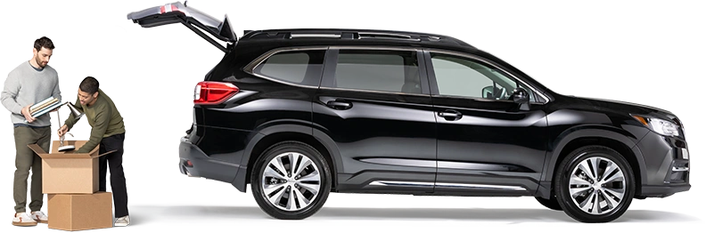 Standing behind a black SUV with open hatch, a pair of roommates pack a lamp and notebooks into a box