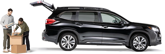 De pie detrás de un SUV negro con la cajuela abierta, un par de compañeros de cuarto empacan una lámpara y cuadernos en una caja.