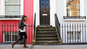 A woman approaches the stairs of a pink apartment building.