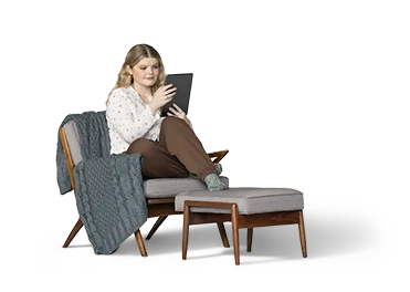 Una joven está recostada en un sillón acolchado gris con reposapiés mientras mira su iPad.