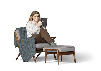 Una joven está recostada en un sillón acolchado gris con reposapiés mientras mira su iPad.