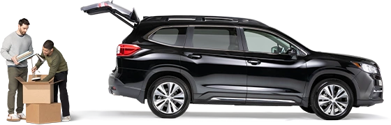 De pie detrás de un SUV negro con la cajuela abierta, un par de compañeros de cuarto empacan una lámpara y cuadernos en una caja.