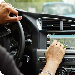 Person in a vehicle, one hand on the steering wheel and one interacting with an onboard telematics device