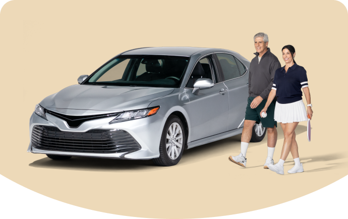 A couple poses near a car dressed in tennis-style outfits